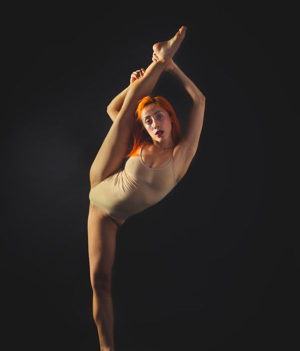 Woman in a dynamic yet controlled stretching pose in a dark studio.